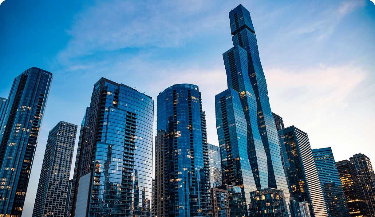 A cluster of modern glass skyscrapers reflecting the sky at sunset, with the tallest building standing prominently among the others.